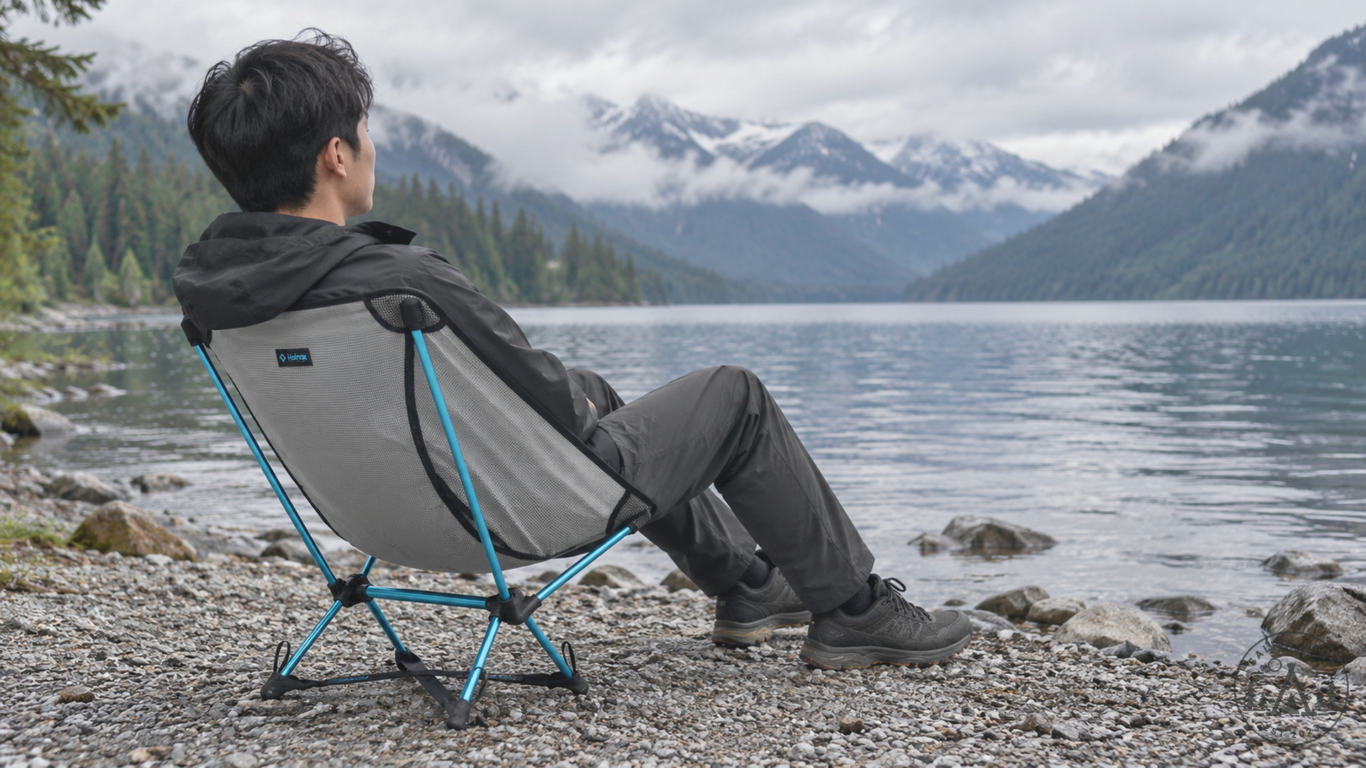 Camper seated in a Cyan Chair Zero LT on a gravel lakeshore below Cascade peaks