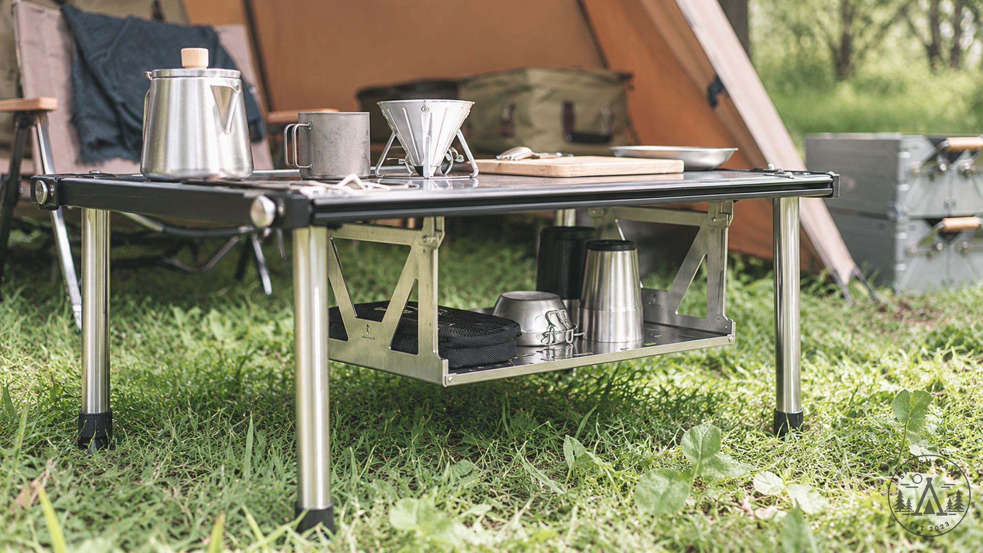 Side view of the stainless shelf under a low table, with camp cookware and a tent around it