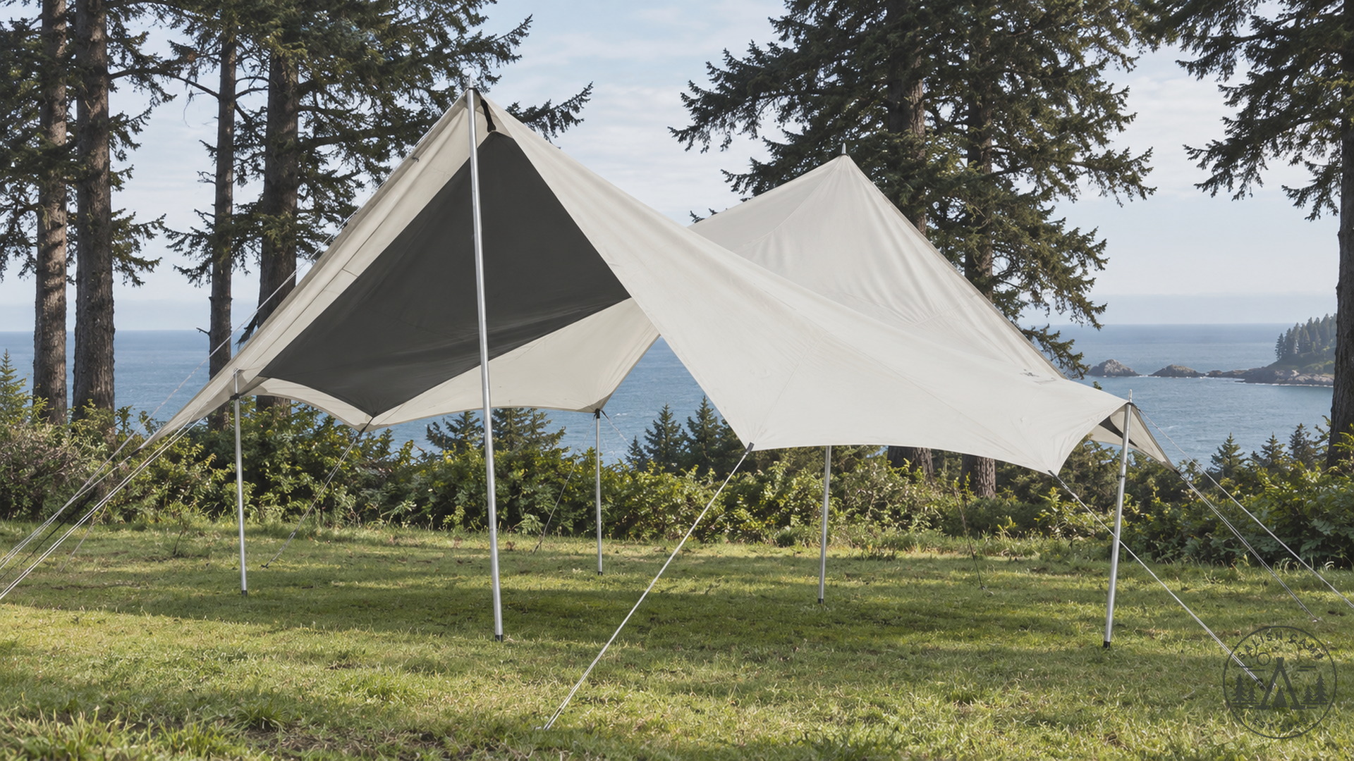 Empty Takibi Tarp Octa pitched on grass by the water, light shell and dark underside, silver poles and guylines, no people
